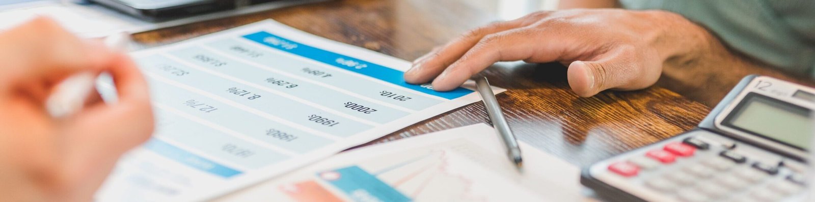 Hands at a desk with financial graphs, calculator, and pen, analysing business data.